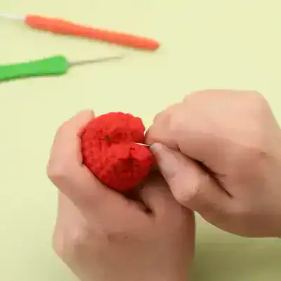 Colorful crochet strawberries, a handmade craft, with crochet hooks and tools in the background. Perfect for DIY enthusiasts and craft lovers.