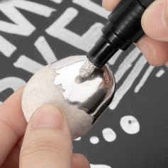 Shiny metallic nail being decorated with a marker for a modern nail art design, showcasing a promotional image for Monalisa Store's nail customization tools.