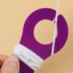 Reusable purple silicone cuticle pusher with attached white string and cotton wrap for manicures and pedicures, ideal for nail care.