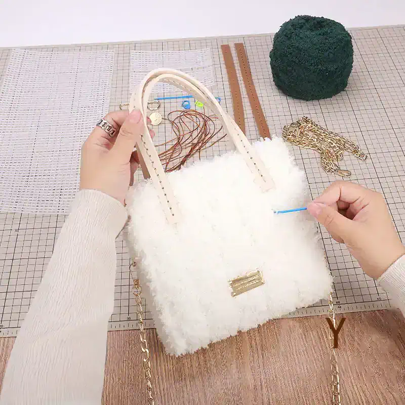 Handbag DIY repair with needle and thread on fluffy white purse, surrounded by tools and accessories on crafting workspace.