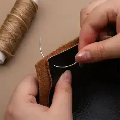 Sewing leather with needle and thread, close-up of hands stitching leather material at Monalisa Store for premium eyewear craftsmanship.