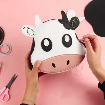 Cute cow-shaped handbag, ideal for children's accessories or playful fashion statements. Made of soft materials with cartoon features, perfect for gifting or casual use.