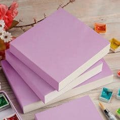 Pink notebooks on a wooden desk with art supplies, perfect for stylish stationery, journaling, and note-taking at Monalisa Store.