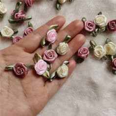 Delicate pink and cream satin rose floral embellishments with green ribbon leaves, ideal for wedding decorations, dress accessories, or craft projects for a luxurious touch.