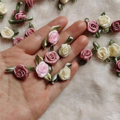 Delicate pink and cream satin rose floral embellishments with green ribbon leaves, ideal for wedding decorations, dress accessories, or craft projects for a luxurious touch.