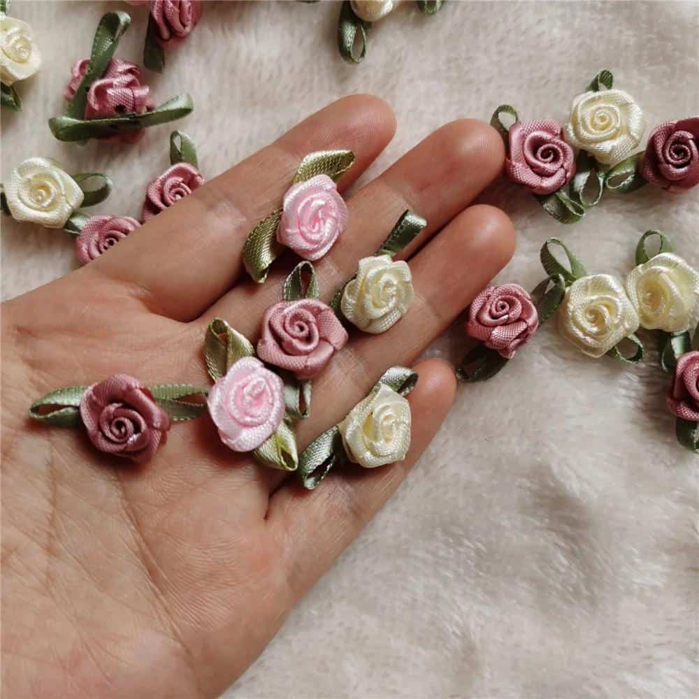 Delicate pink and cream satin rose floral embellishments with green ribbon leaves, ideal for wedding decorations, dress accessories, or craft projects for a luxurious touch.