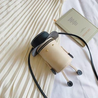 Miniature designer handbag with shoulder strap, beige and black color, stylish accessory for women, displayed on a soft fabric surface.