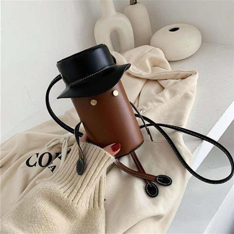Coffee mug with a black leather hat, set against a minimalist background with white decorative objects and a cream-colored blanket, showcasing trendy accessories from Monalisa Store.