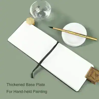 Elegant white notebook with black elastic strap, gold pen, glass of water, and ceramic dish on a gray surface for artistic sketching and handwriting at Monalisa Store.