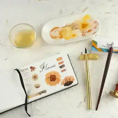Watercolor watercolor brushes and flowers sketchbook on a white textured surface.