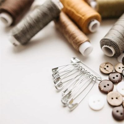 Colorful sewing threads, safety pins, and buttons on a white background, symbolizing sewing supplies for fashion, tailoring, and craft projects.