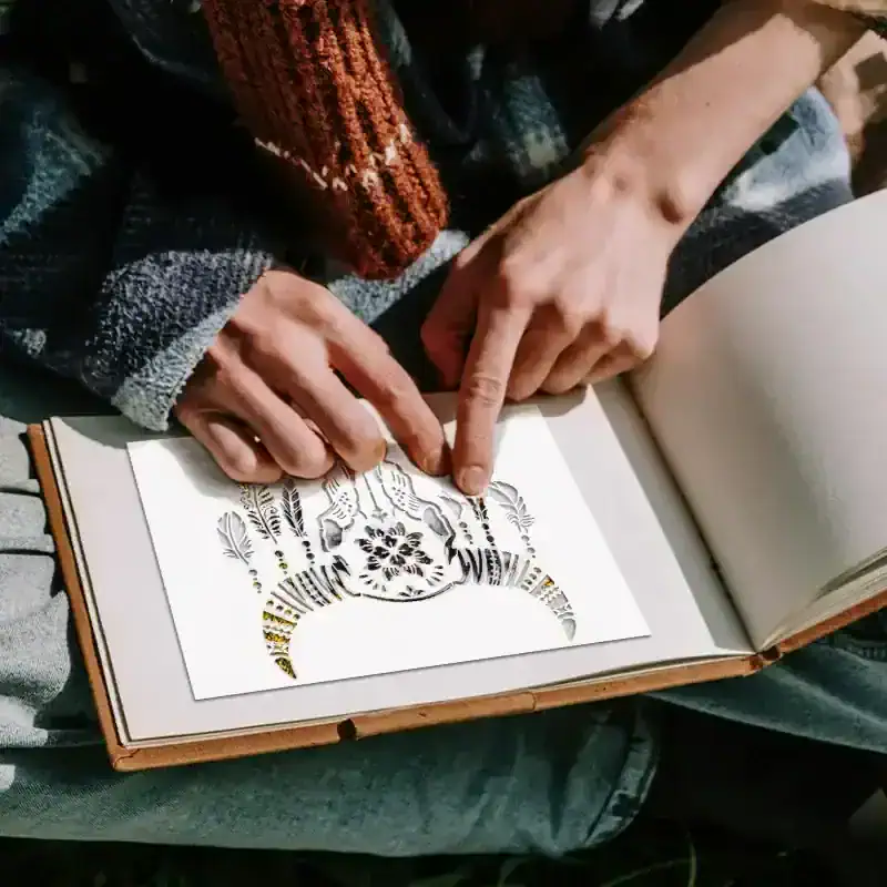 Intricate paper cut art showcased with a person pointing to detailed design, emphasizing craftsmanship and artistry in paper crafting.