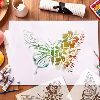 Vibrant butterfly stencil art with floral patterns on white paper, surrounded by watercolor paints, brushes, and art supplies, showcasing creative painting techniques at Monalisa Store.