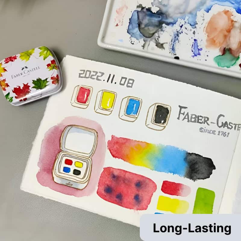 Vibrant watercolor palette and Faber-Castell stationery on art project paper, showcasing colorful artistic supplies for creative expression and watercolor painting.