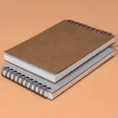 Spiral notebooks with brown, white, and gray covers on a peach background, symbolizing organization and note-taking for those interested in optical and eyewear solutions.