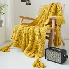 Luxurious yellow chunky knit throw blanket draped over wooden armchair in cozy home setting with vintage-inspired portable radio nearby, perfect for relaxing spaces.