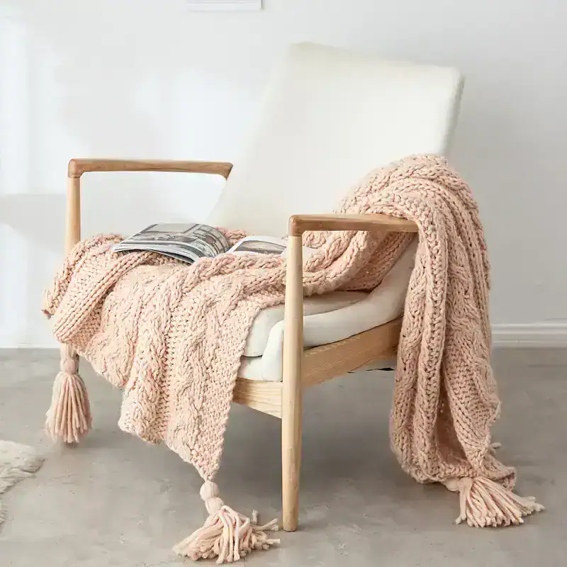 Soft pink chunky knit throw blanket draped over a modern white chair in a cozy, stylish space. Perfect for home decor or relaxation, adding warmth and texture.