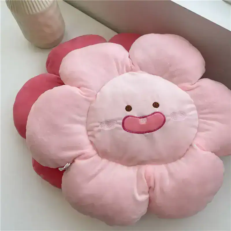 Soft pink flower-shaped plush cushion with a cute smiling face, perfect for kids' rooms or cozy decor.
