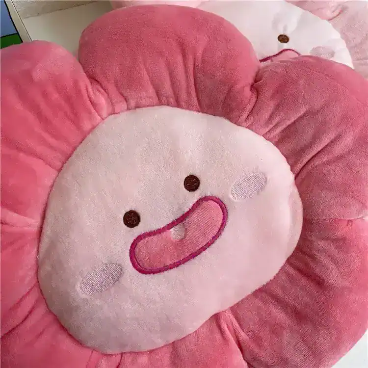 Cute pink flower-shaped plush pillow with a smiling face, perfect for kids and home decor. Soft and comfortable, ideal for bedroom accessories or playful gifts.
