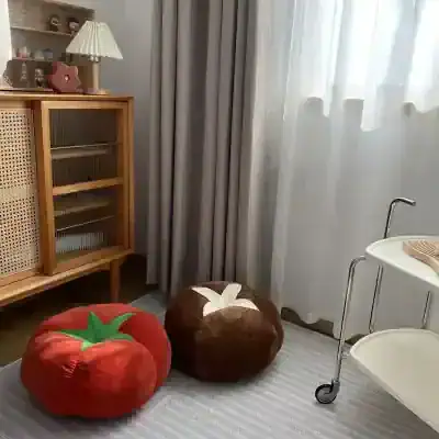 Plush tomato and pumpkin-shaped cushions in cozy bedroom corner, with natural light, bedside cabinet, and decorative accessories for comfortable living and stylish interior design.