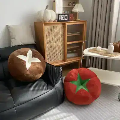 Fruit-themed plush pillows on a black leather sofa, cozy home decor, perfect for living room comfort, featuring tomato and pumpkin designs, with a wooden cabinet and modern side table in the background.