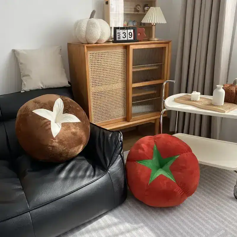 Fruit-themed plush pillows on a black leather sofa, cozy home decor, perfect for living room comfort, featuring tomato and pumpkin designs, with a wooden cabinet and modern side table in the background.