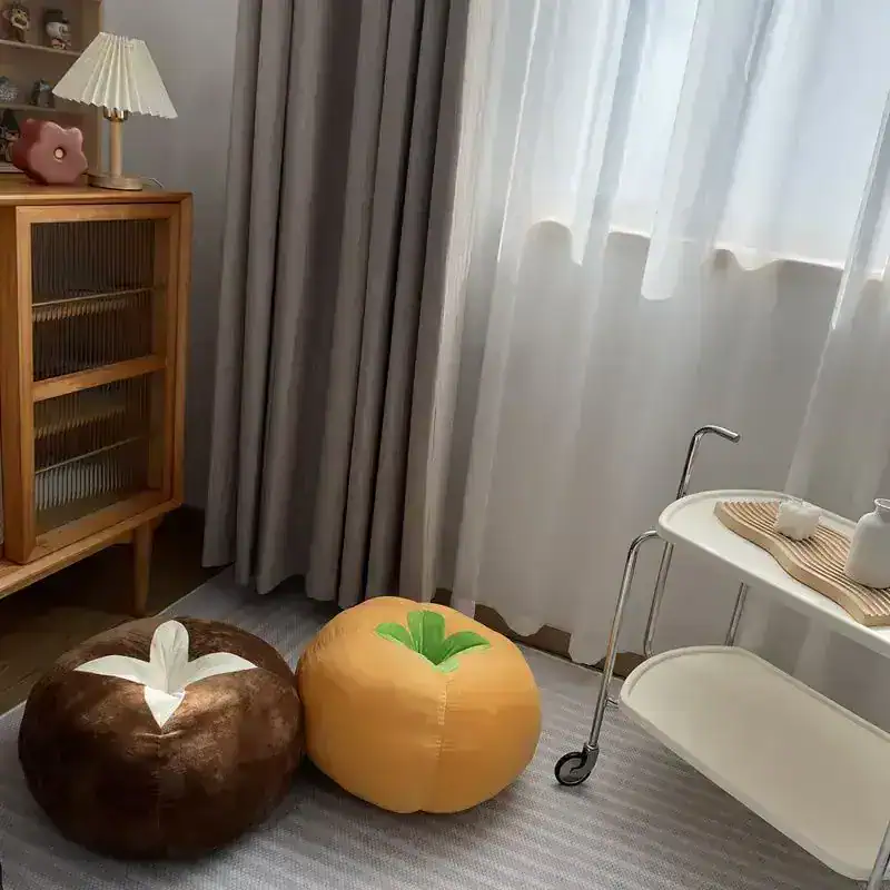 Soft gray curtains in a bright, modern room with cozy plush fruit-shaped cushions and a sleek white cart, perfect for relaxing or skincare treatments.