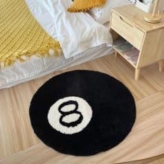 Round black and white yoga rug with a Monet-inspired design, placed on wooden flooring next to a bed with a yellow throw and a wooden bedside table with slippers.