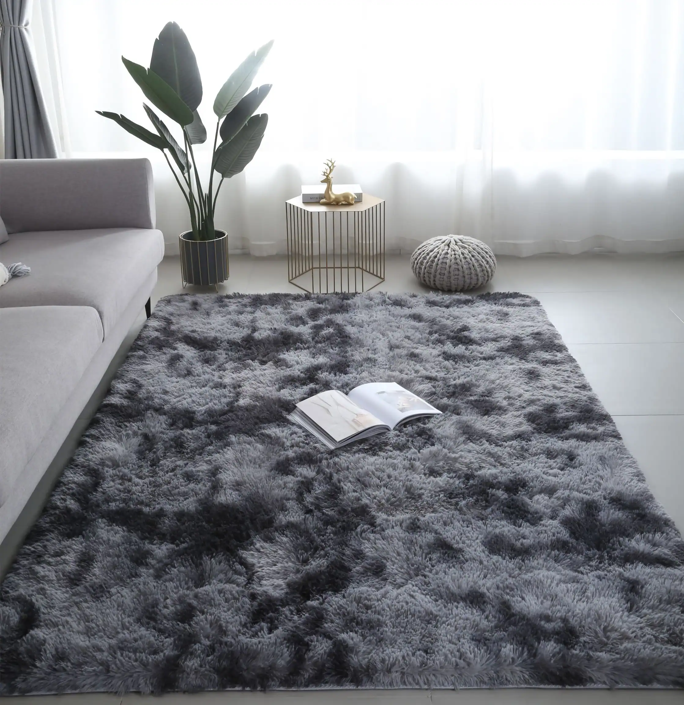Luxurious gray plush area rug in a modern living room with natural light, minimal decor, and a cozy reading corner featuring a stylish sofa, potted plant, and decorative accents.
