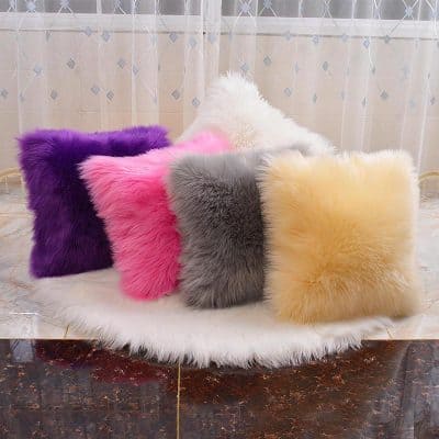 Colorful faux fur throw pillows in purple, pink, gray, cream, and white on a white furry rug, ideal for stylish home decor and cozy comfort.
