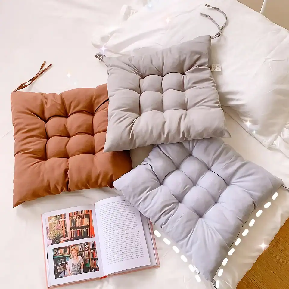 Soft tufted decorative pillows in tan, gray, and light gray colors on a bed with a white duvet, next to an open book about bookshelves, perfect for cozy home decor.