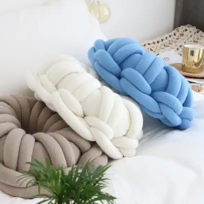 Soft braided slippers in beige, white, and blue, displayed on a bed for comfortable indoor wear, perfect for relaxation.