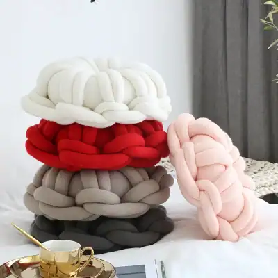 Soft plush knot pillow in white, red, light pink, beige, and black colors, decorative home accessory for modern interior decor.