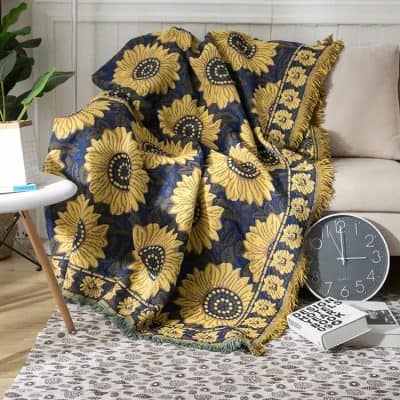 Sunflower patterned throw blanket with navy blue background, placed on a beige sofa in a modern living room setting.