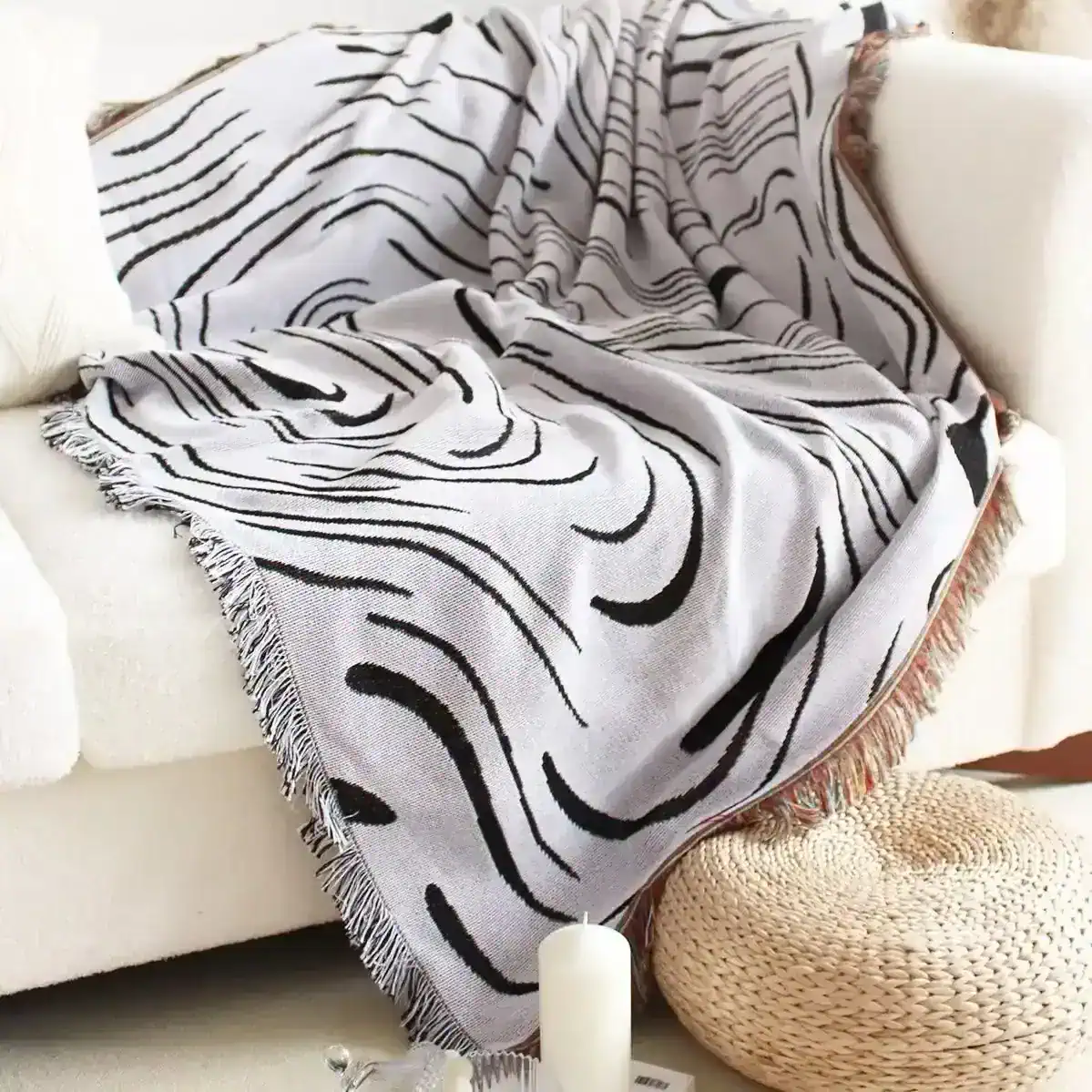 Luxurious black and white patterned throw blanket draped over a plush cream sofa, with cozy decorative pillows, candle, and woven ottoman, perfect for stylish home décor and comfort.