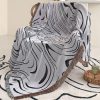 Vibrant black and white abstract patterned throw blanket draped over a chair with fringed edges, adding modern style to home decor.