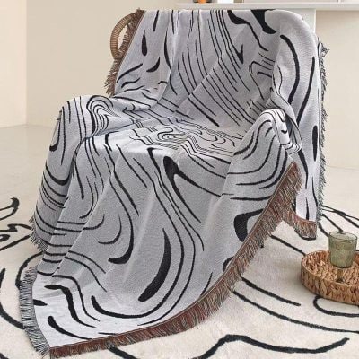 Vibrant black and white abstract patterned throw blanket draped over a chair with fringed edges, adding modern style to home decor.