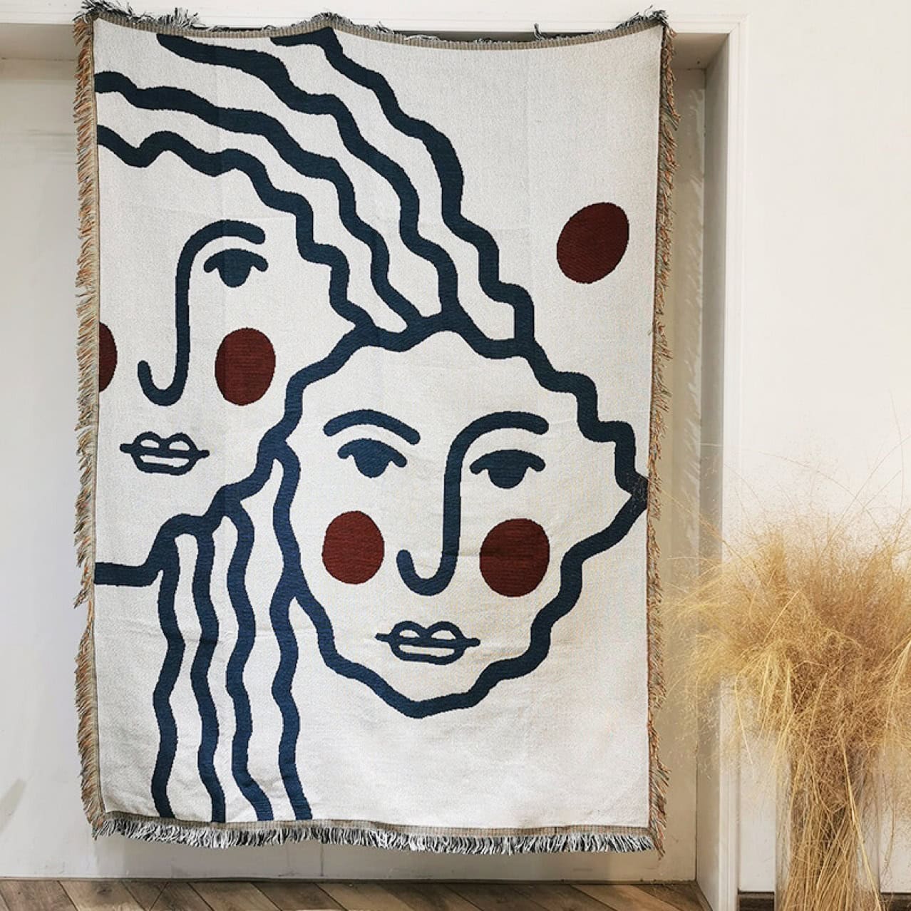 Intricate textile wall art featuring abstract line art faces with bold blue and red accents, perfect for modern home decor and adding artistic flair to any space.