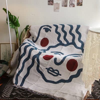 Bold abstract face art blanket featuring blue and red lines, draped over a couch in a modern living room. Perfect for adding artistic flair to your home decor.