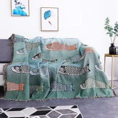 Colorful fish-patterned throw blanket draped over gray sofa in modern living room with framed artwork and houseplant, showcasing stylish home decor.
