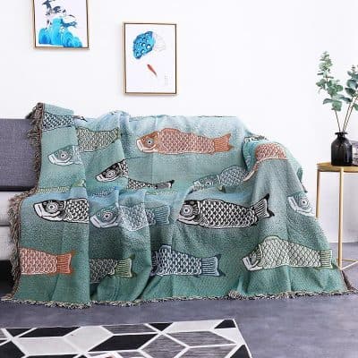 Colorful fish-patterned throw blanket draped over gray sofa in modern living room with framed artwork and houseplant, showcasing stylish home decor.