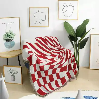 Soft modern living room with a red and white geometric patterned throw blanket, surrounded by minimalist art prints and a large green indoor plant, creating a cozy and stylish space.