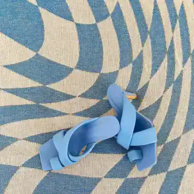 Flat lay of trendy blue rubber sandals on a geometric patterned rug, perfect for summer fashion and casual footwear collections at Monalisa Medical Store.