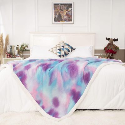 Colorful tie-dye fleece blanket draped over a white bed with Christmas decorations and modern decor in a cozy bedroom.