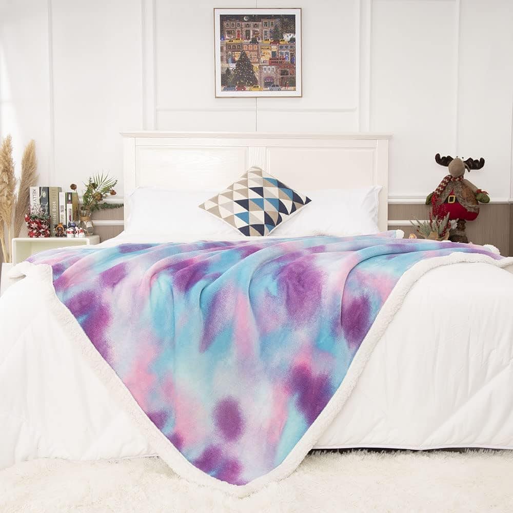 Colorful tie-dye fleece blanket draped over a white bed with Christmas decorations and modern decor in a cozy bedroom.