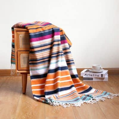 Brightly colored striped towel or throw blanket, ideal for home decor, lounging, or as a gift, featuring vibrant patterns and soft fabric, displayed on wooden furniture with a cozy setting.