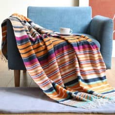 Vibrant colorful striped blanket draped over a stylish blue sofa with a coffee cup on top, perfect for home decor, comfort, and warmth.