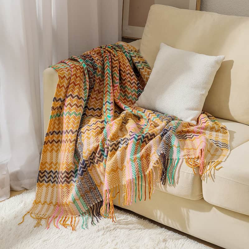 Colorful woven throw blanket with zigzag pattern draped over cream sofa, cozy home decor accessory.