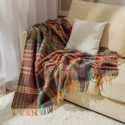 Vibrant multicolored woven throw blanket with fringe, draped over cream sofa with pillows, ideal for cozy home decor.