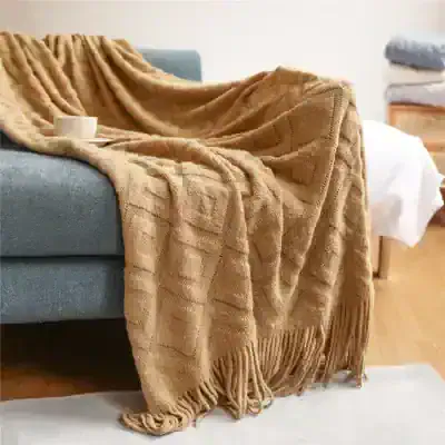 Luxurious beige knitted throw blanket draped over a blue sofa, perfect for cozy comfort and home decor. Soft and plush, ideal for adding warmth to living rooms or bedrooms.